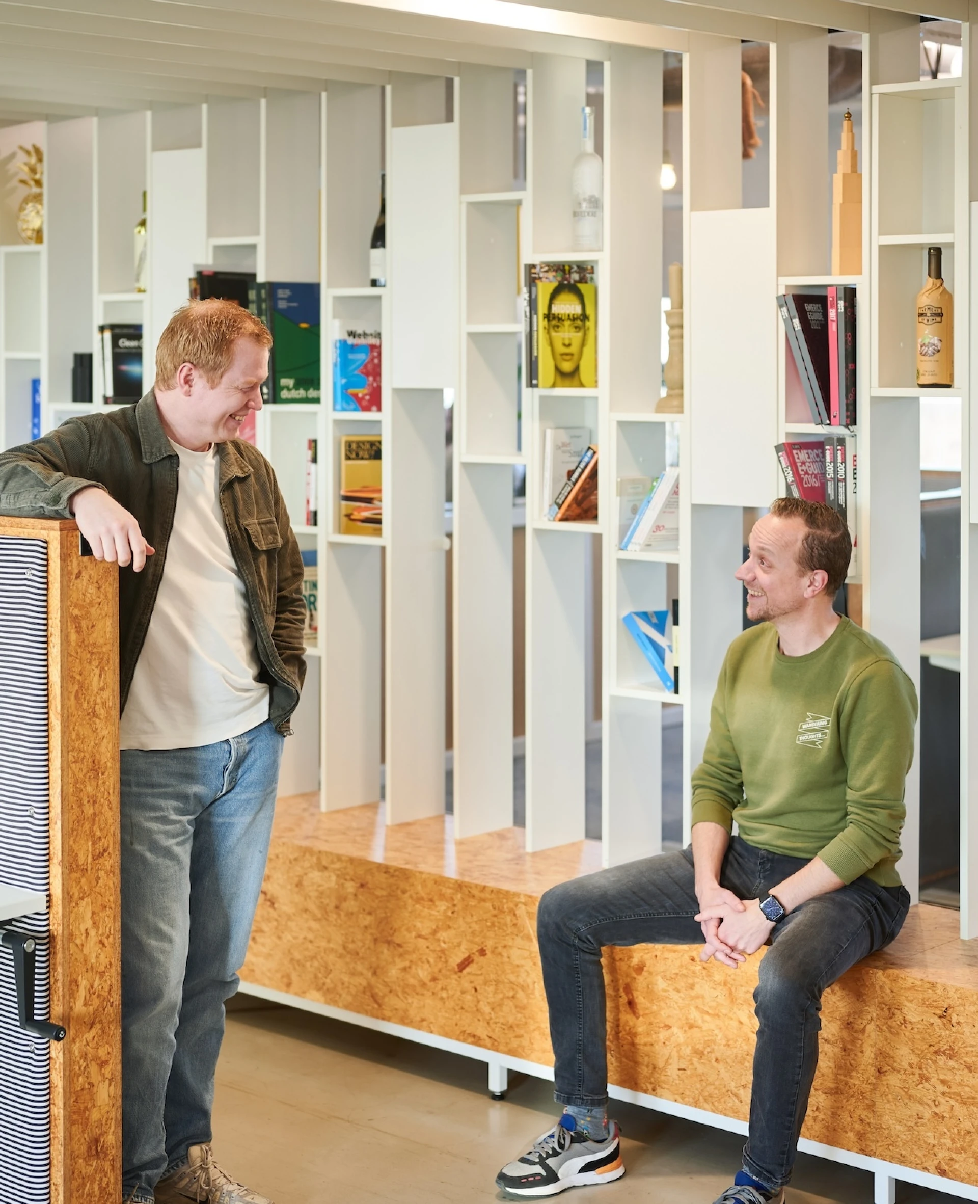 Twee mannen in gesprek in een moderne bibliotheekruimte.
