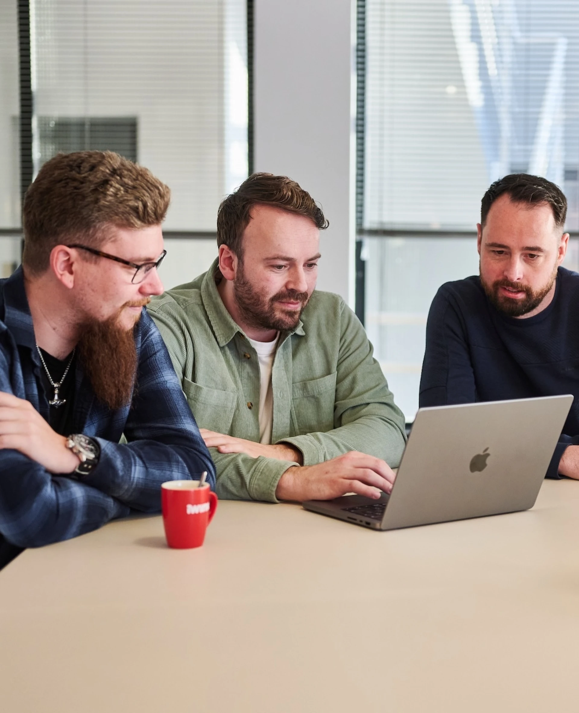 Drie mannen aan een tafel kijken samen naar een laptop.