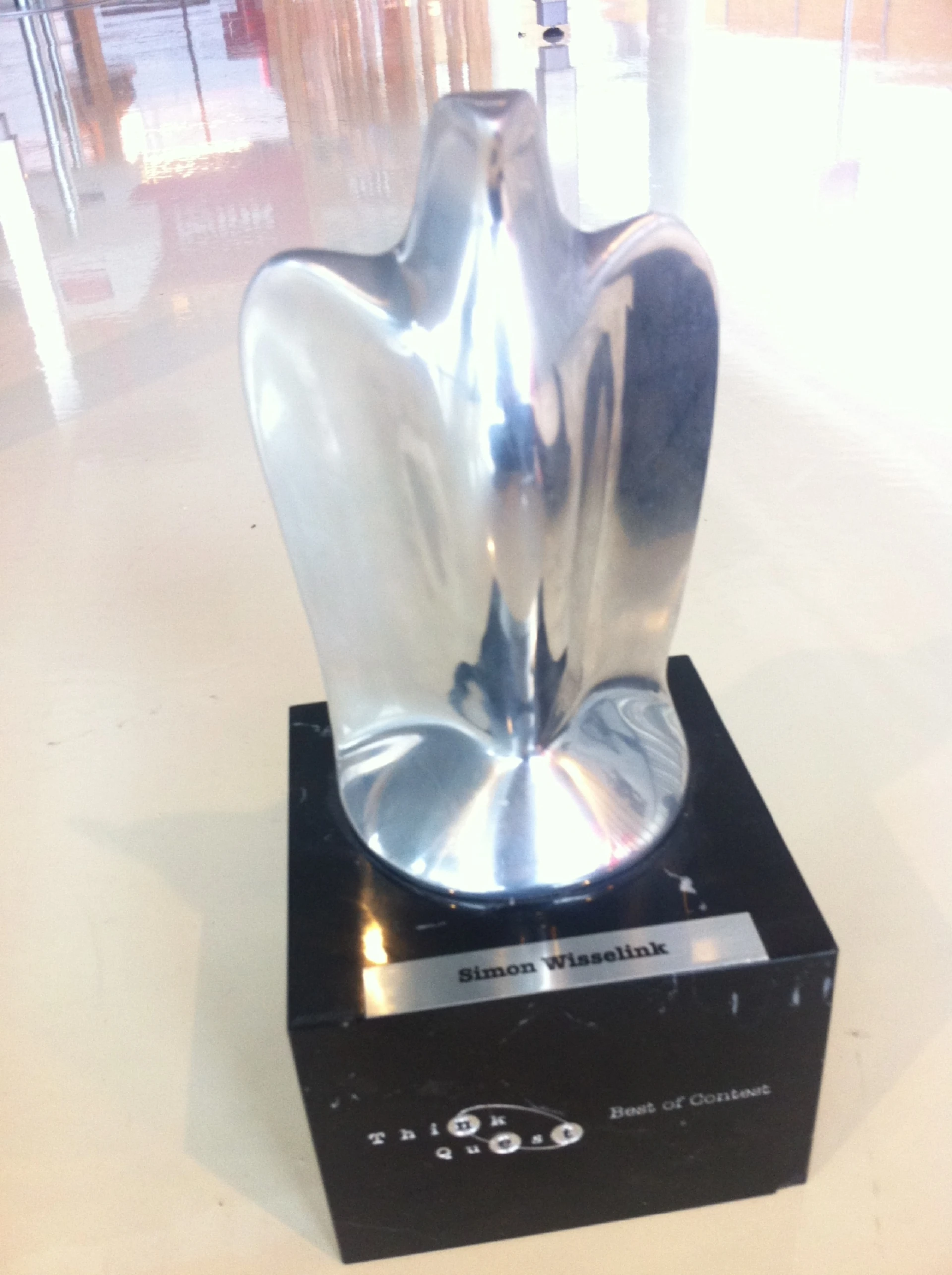 Een zilveren trofee met een abstracte vorm.