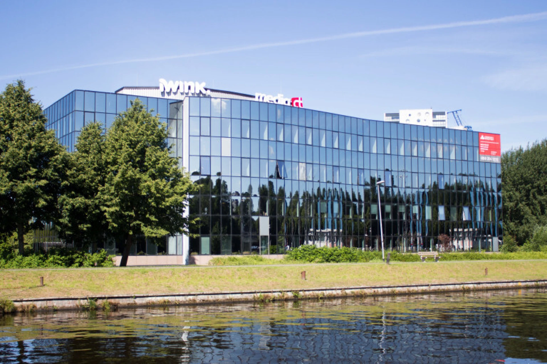 Modern kantoor aan het water met glazen gevels en omliggende bomen.
