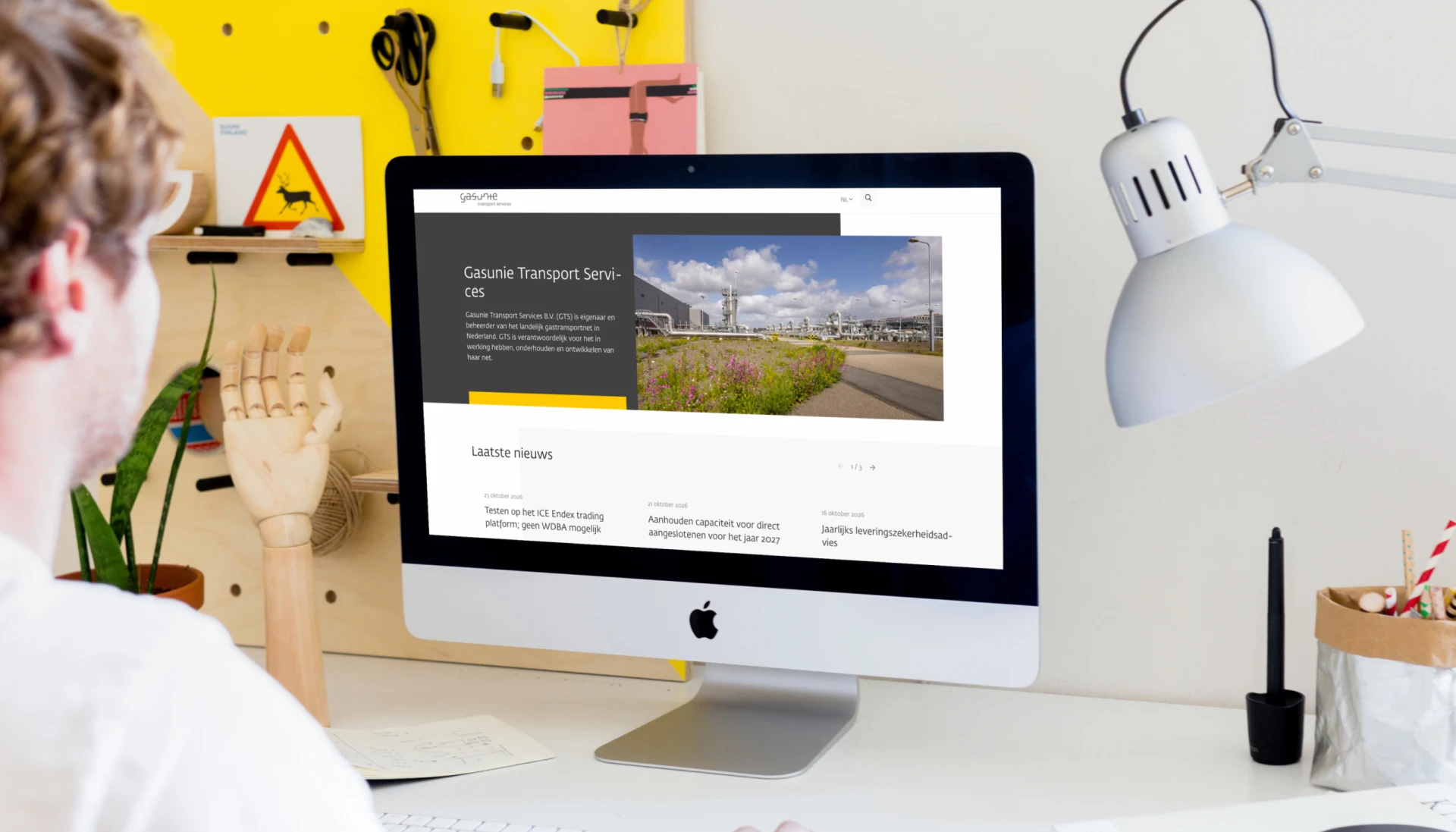 Persoon werkt aan een computer met een website geopend, omringd door bureau-accessoires.