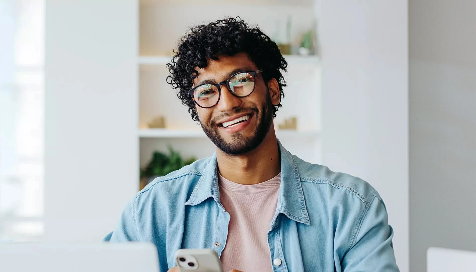 Een glimlachende persoon met een bril houdt een smartphone vast.