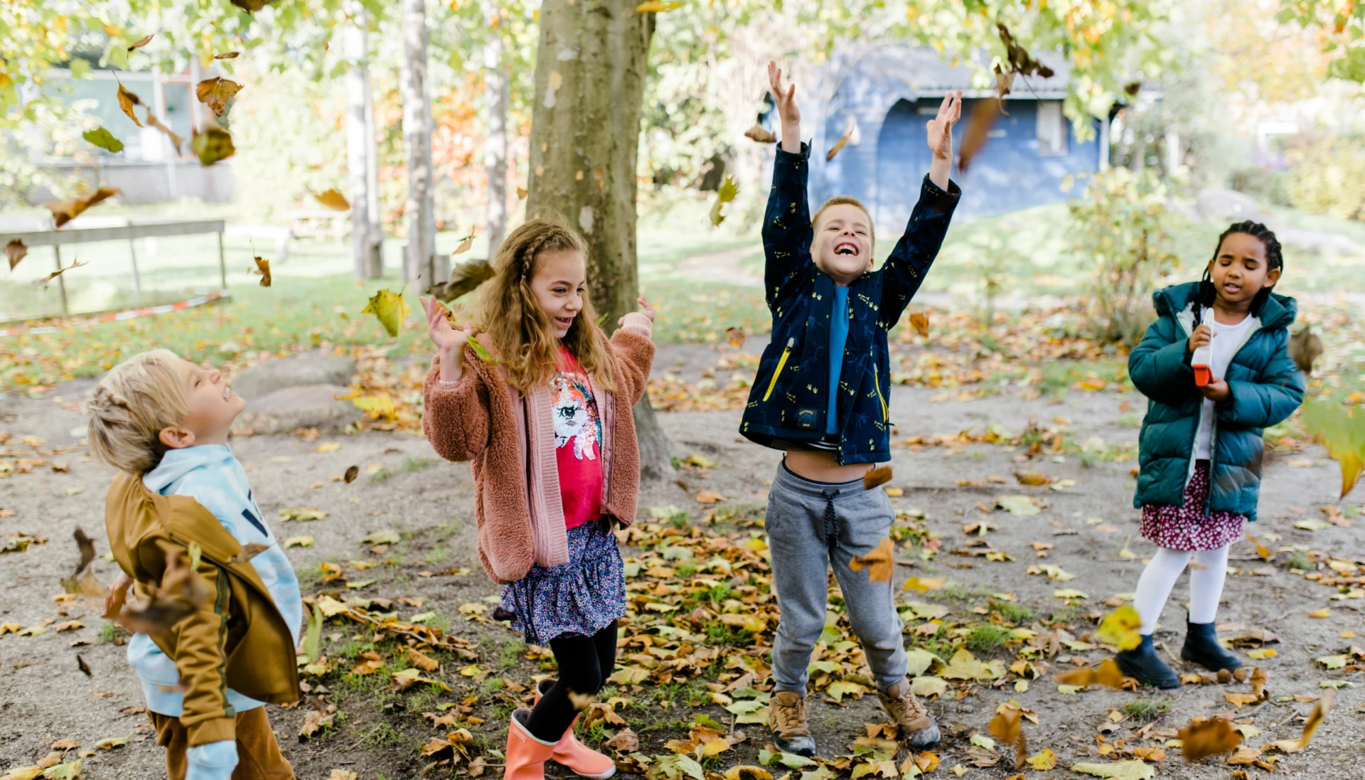 Kinderen spelen en gooien bladeren in een herfstsfeer.
