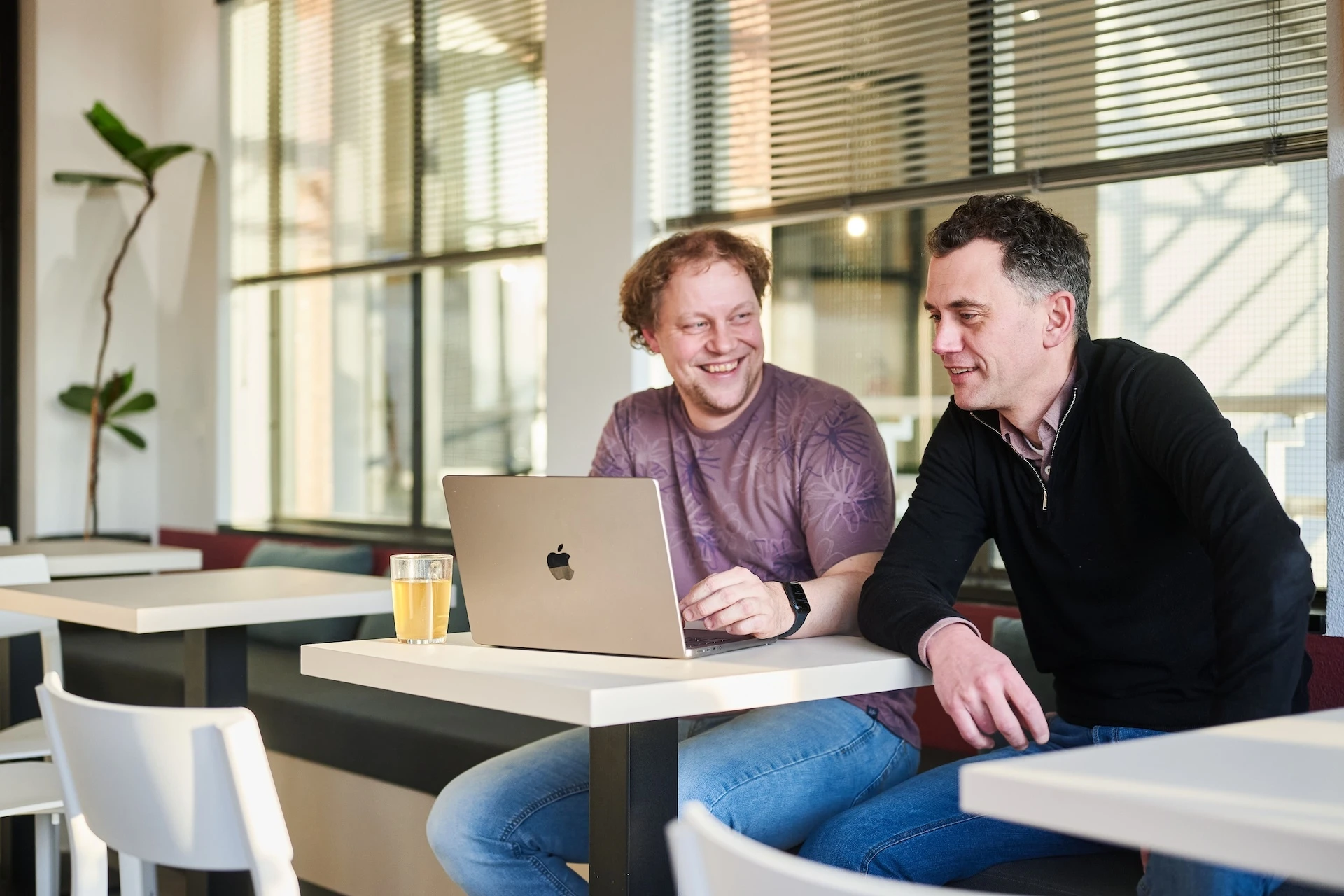 Twee mannen zitten in een gezellige ruimte te werken op een laptop.