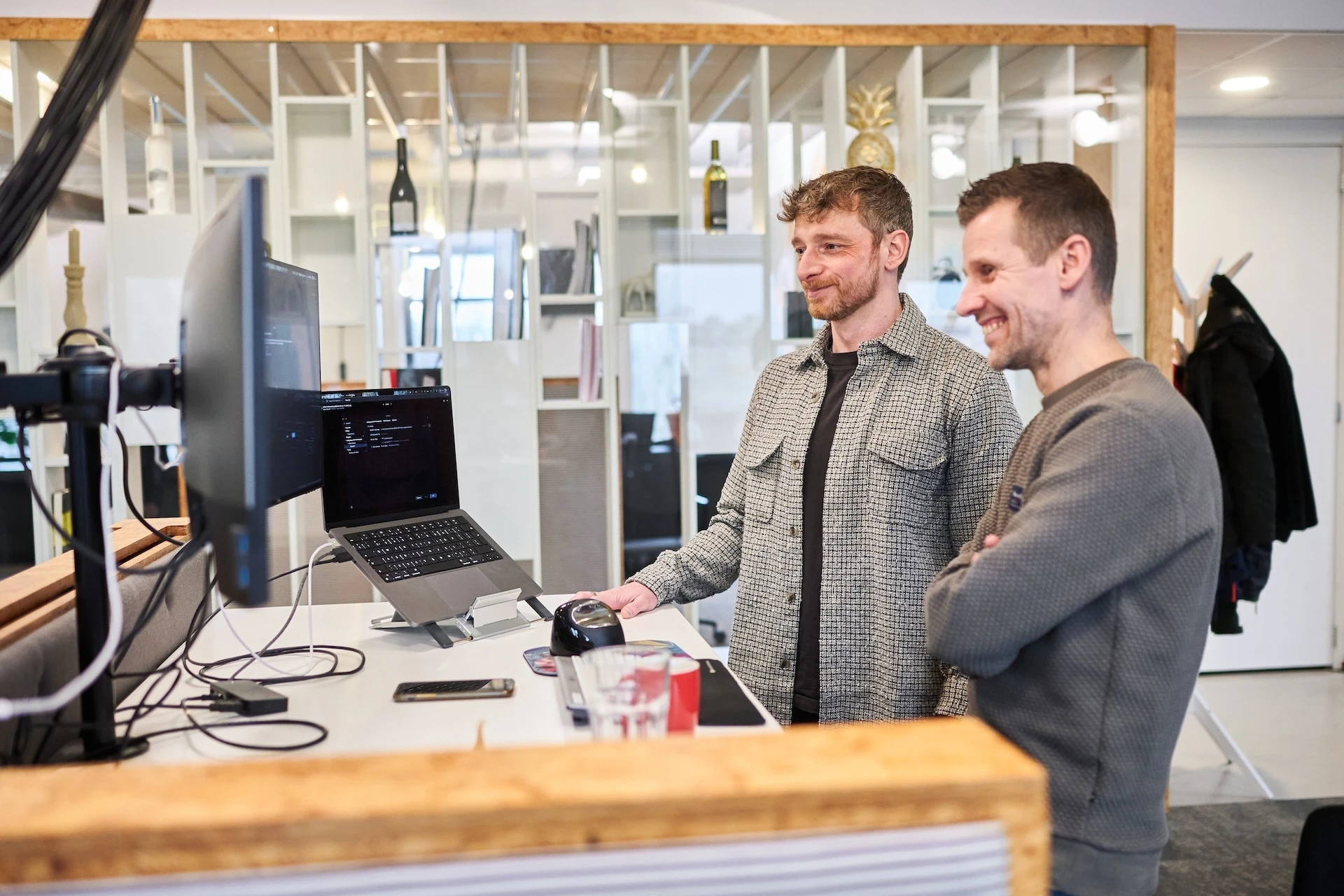 Twee mannen werken samen aan een computerbureau in een moderne kantoorsetup.