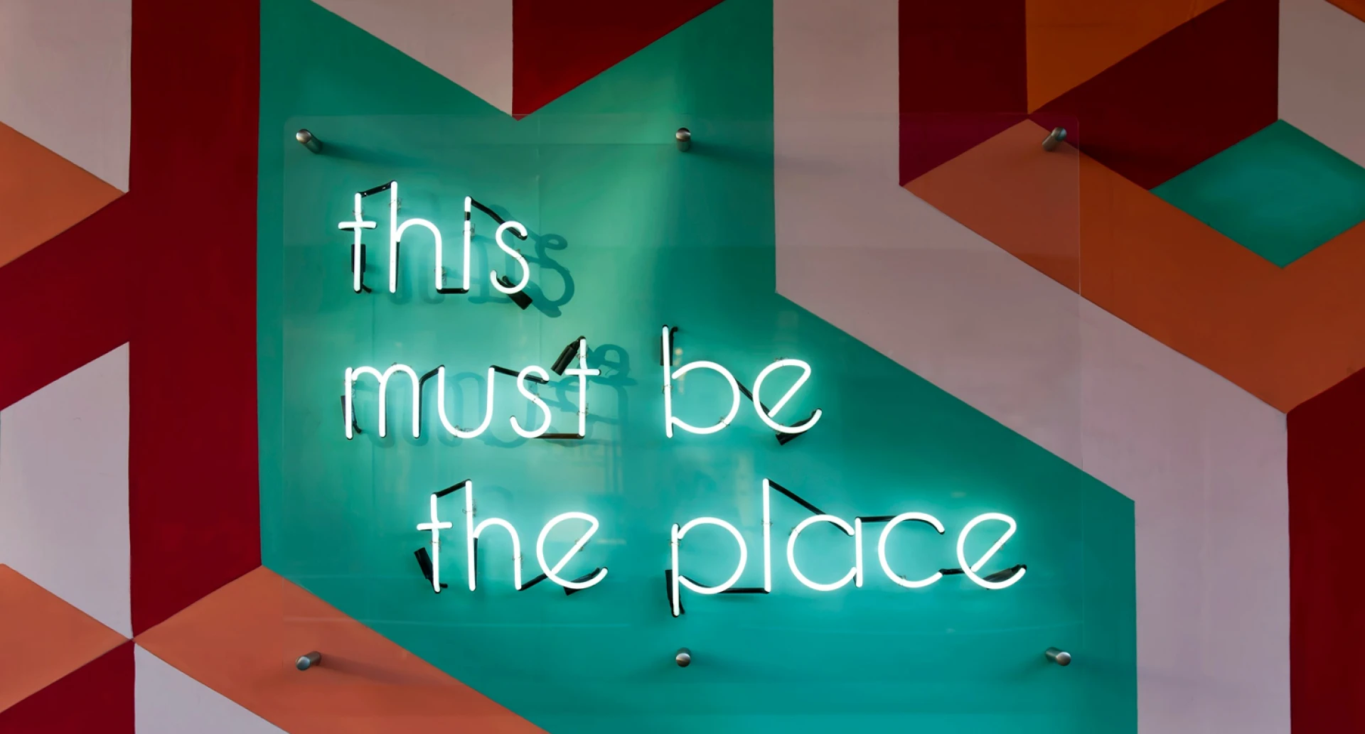 Neonbord met de tekst "this must be the place" op een kleurrijke muur.