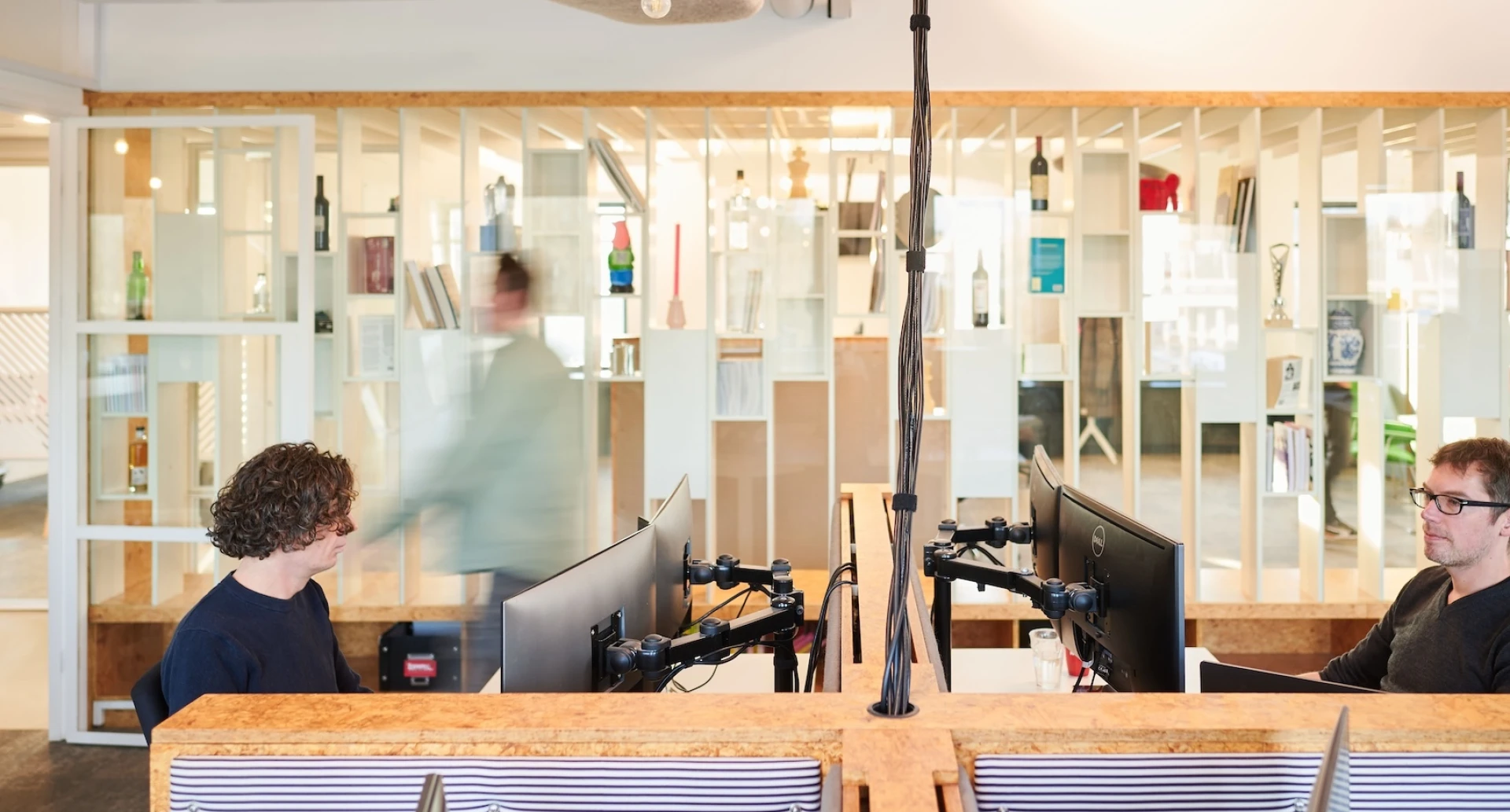 Twee mensen werken achter computerschermen in een modern ingericht kantoor.