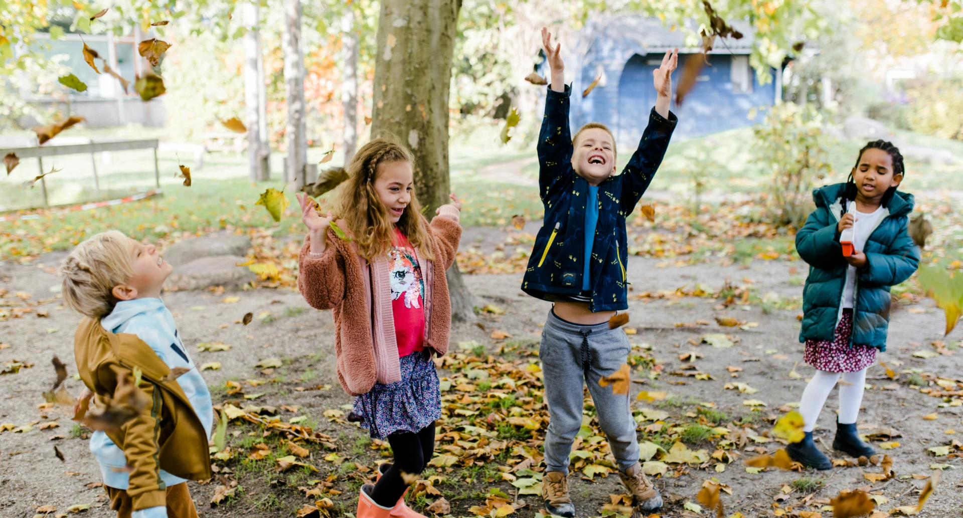Kinderen spelen en gooien bladeren in een herfstsfeer.
