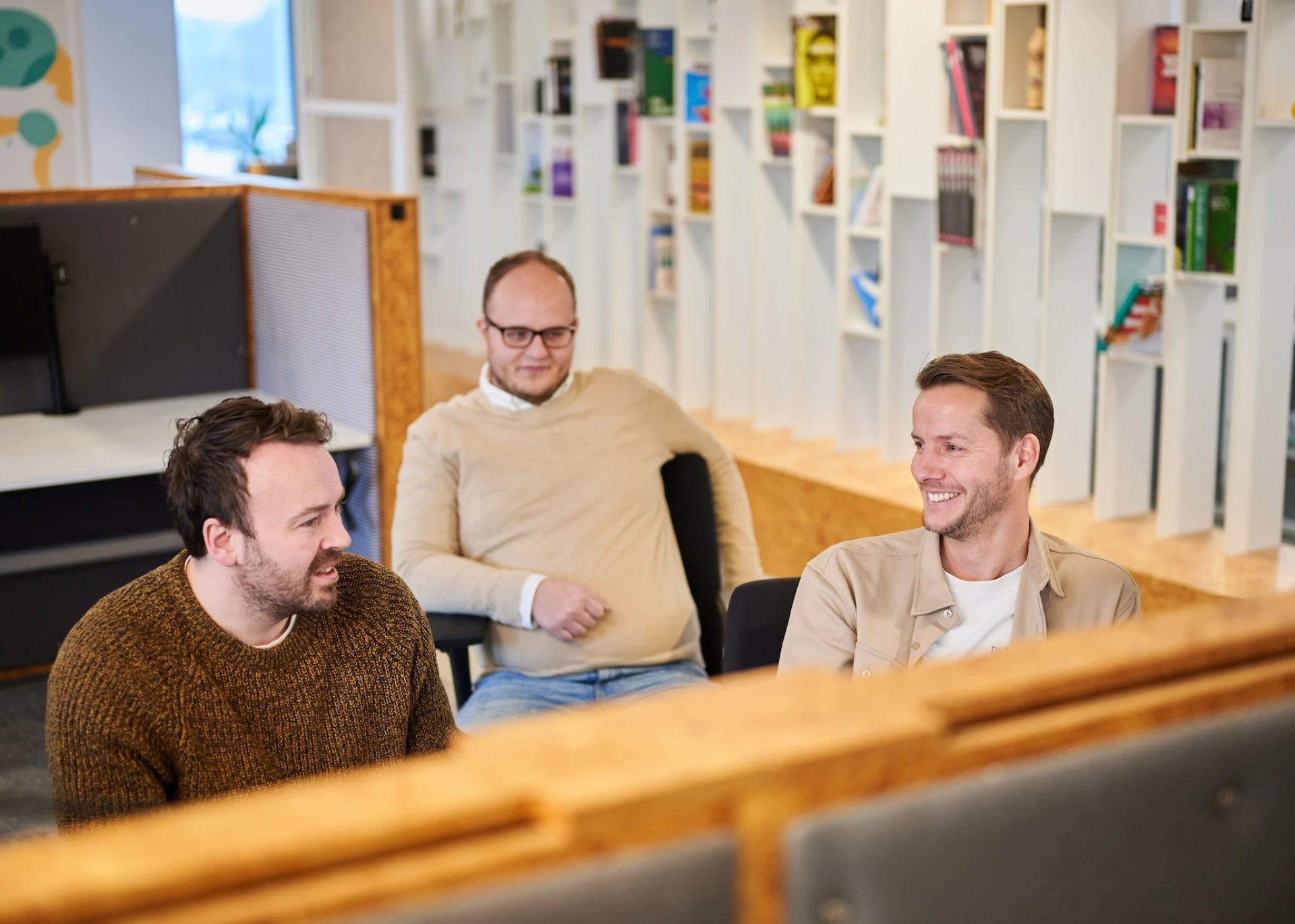 Drie mannen praten en lachen in een moderne kantooromgeving.