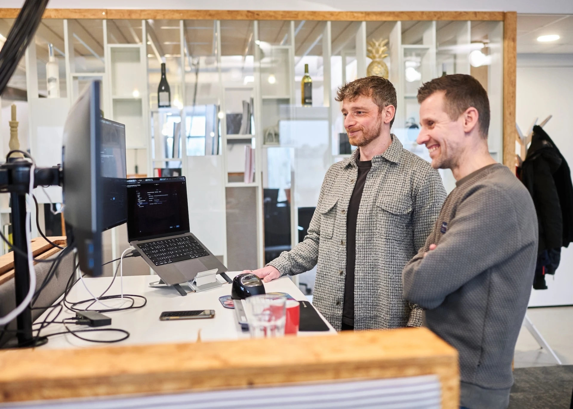 Twee mannen werken samen aan een computerbureau in een moderne kantoorsetup.