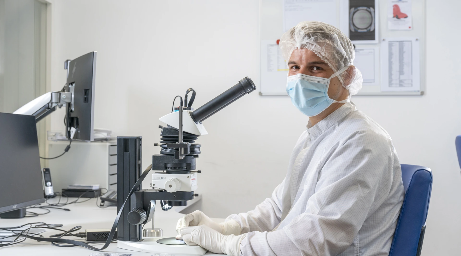 Een laboratoriummedewerker met mondmasker en handschoenen werkt aan een microscoop.