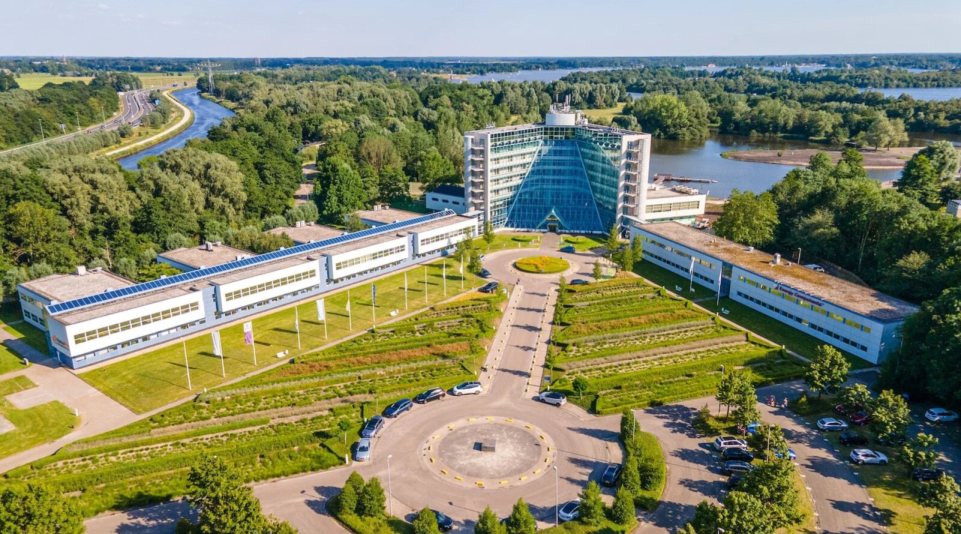 Luchtfoto van een modern gebouw omgeven door groen en waterwegen.
