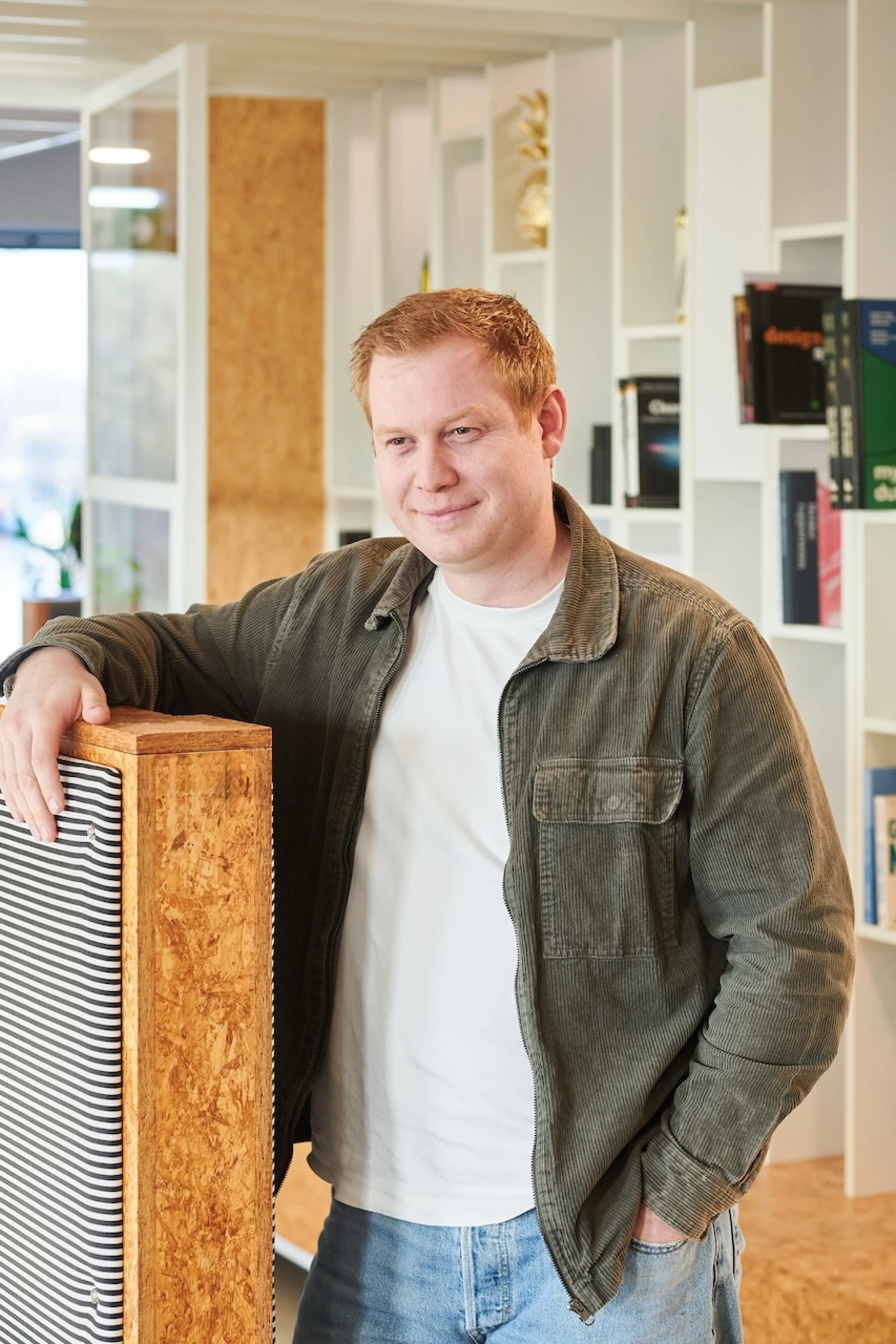 Een man poseert in een modern kantoor met boekenplanken op de achtergrond.