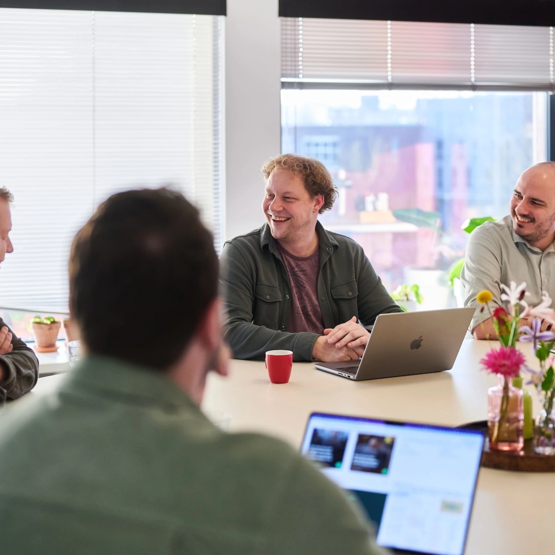 Vergadering met diverse mensen aan tafel met laptops.