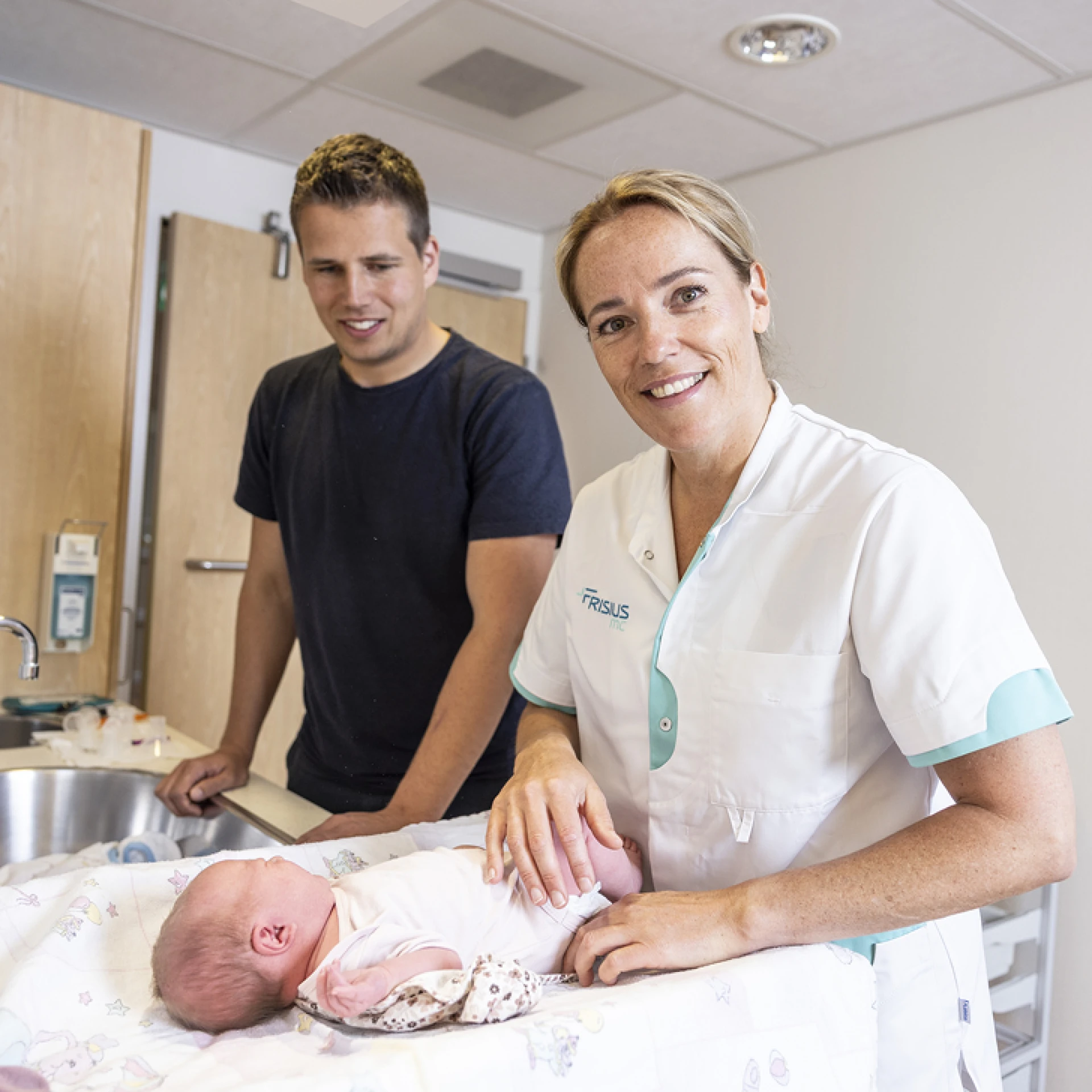 Een verpleegkundige verzorgt een pasgeboren baby met een glimlach terwijl een man toekijkt.