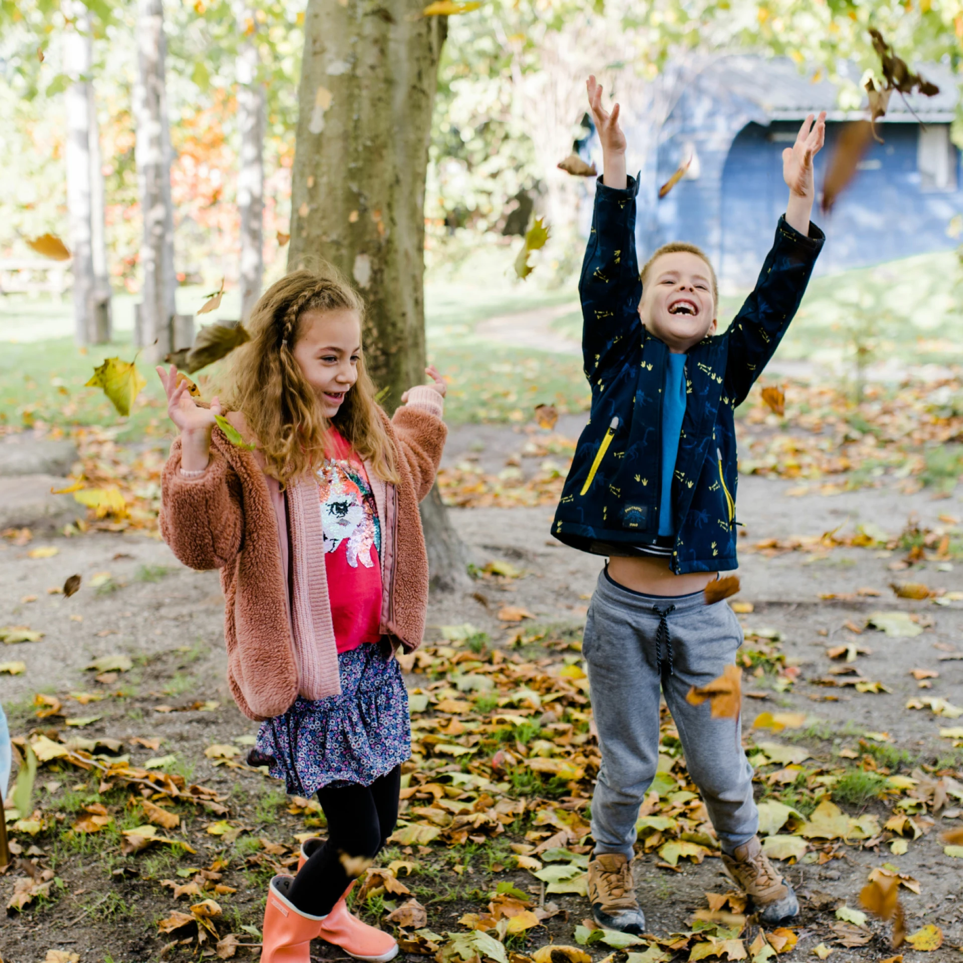 Kinderen spelen en gooien bladeren in een herfstsfeer.